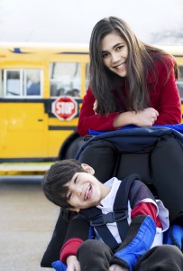 Big sister with disabled brother in wheelchair by school bus