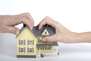 Two hands gripping a yellow model house with grey roof