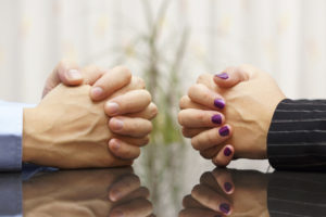 Man and woman sits at a desk with hands clasped.