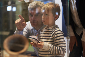 Father And Son Look At Artifacts In Case On Trip To